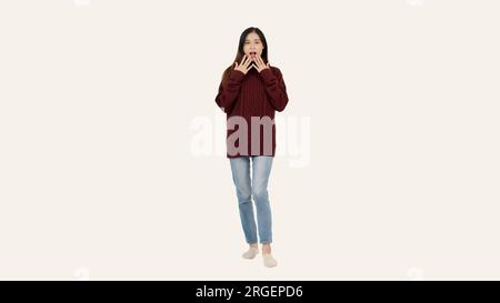 A beautiful young Asian woman in a cozy red sweater poses with a shocked, stunned face, standing against an isolated white background. Stock Photo