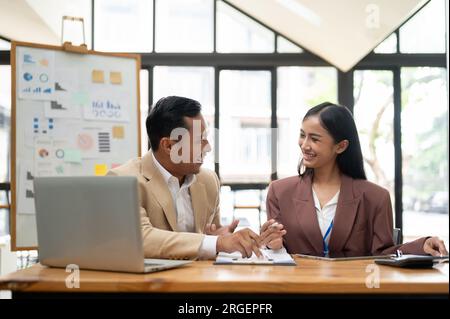 A happy and professional Asian businessman is sharing ideas, brainstorming, and working with a female colleague on a project in the office. Stock Photo