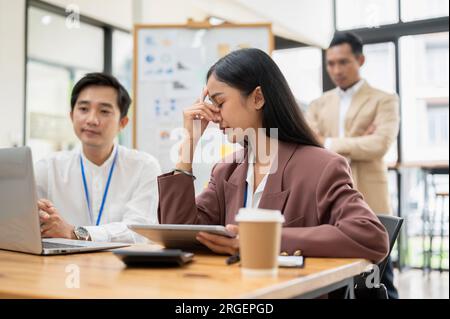 A stressed Asian businesswoman worried about her project tried to fix a project problem with her colleague in the office. Stock Photo