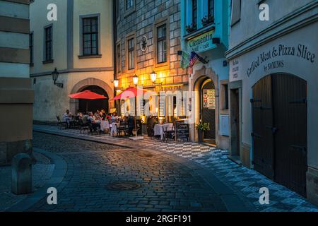 Small outdoor restaurant on the narrow cobblestone street illuminated by lights in old town of Prague, Czech Republic. Stock Photo
