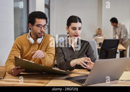 Portrait of two young Middle Eastern professionals man and woman using laptop together in modern office discussing business projects, copy space Stock Photo
