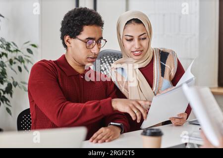 Two modern Arabian business people man and woman working together at meeting table in office and discussing documents Stock Photo