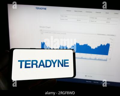 Person holding mobile phone with logo of American test equipment company Teradyne Inc. on screen in front of web page. Focus on phone display. Stock Photo