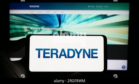 Person holding cellphone with logo of US test equipment company Teradyne Inc. on screen in front of business webpage. Focus on phone display. Stock Photo