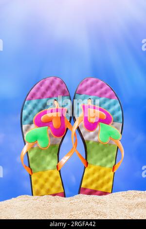 Multi colored flip flops, slates with heart on sand. Sunny day. Vacation, sea, Valentine's day on beach. Vertical. Copy space Stock Photo