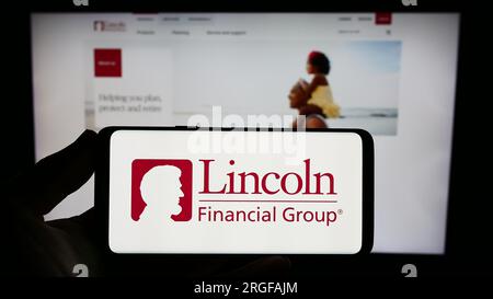 Person holding smartphone with logo of US financial company Lincoln National Corporation on screen in front of website. Focus on phone display. Stock Photo