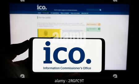 Person holding cellphone with logo of British Information Commissioner's Office (ICO) on screen in front of webpage. Focus on phone display. Stock Photo