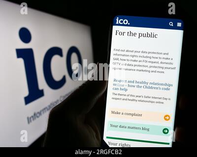 Person holding cellphone with website of British Information Commissioner's Office (ICO) on screen with logo. Focus on center of phone display. Stock Photo