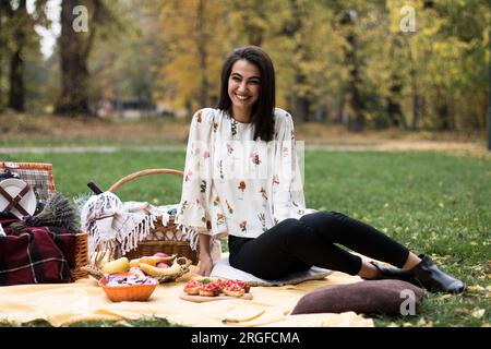 Young beautiful happy woman on a picnic in the park, waiting for her friends to arrive. Stock Photo