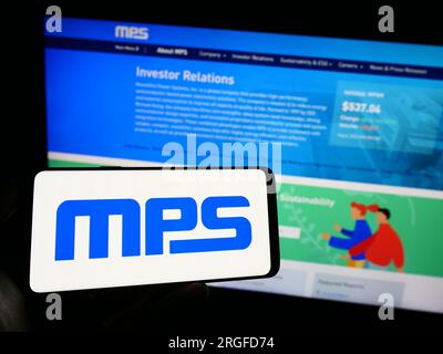 Person holding mobile phone with logo of US company Monolithic Power Systems Inc. (MPS) on screen in front of web page. Focus on phone display. Stock Photo