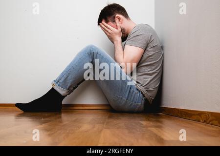 depressed man sitting in a corner of a room Stock Photo - Alamy