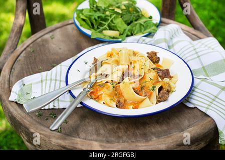 Pasta tagliatelle spaghetti with creamy sauce served on plate outside on sunny day. Eating fresh fettucine or pappardelle with meat in creamy sauce. Stock Photo