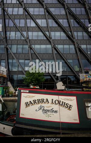 London, UK: Canal boat on the Paddington branch of the Grand Union Canal at Paddington Basin with modern building behind. Stock Photo