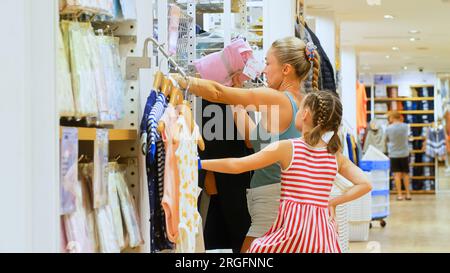 Cute shopaholic mom and daughter choose looking for clothes in clothing store. Mom and daughter shopper customer is looking and buying casual clothes in clothing store. Concept shopping clothes store ...