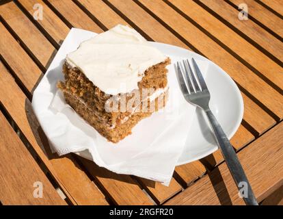 A piece of carrot cake on a white plate against a wooden table background Stock Photo