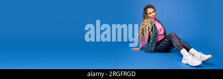 full length of long haired african american woman in sporty outfit sitting on blue, banner Stock Photo