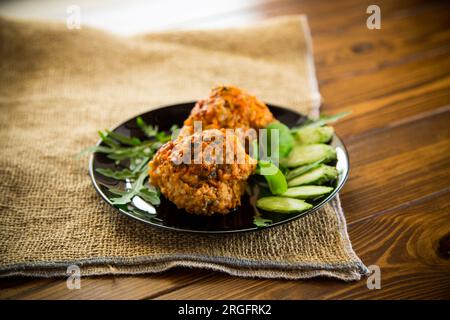 Cooked meatballs in a plate with fresh vegetables, on a wooden table. Stock Photo