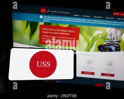 Person holding smartphone with logo of Universities Superannuation Scheme (USS) on screen in front of website. Focus on phone display. Stock Photo