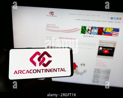 Person holding smartphone with logo of company Arca Continental S.A.B. de C.V. on screen in front of website. Focus on phone display. Stock Photo