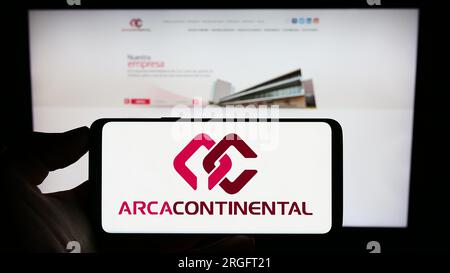Person holding cellphone with logo of company Arca Continental S.A.B. de C.V. on screen in front of business webpage. Focus on phone display. Stock Photo