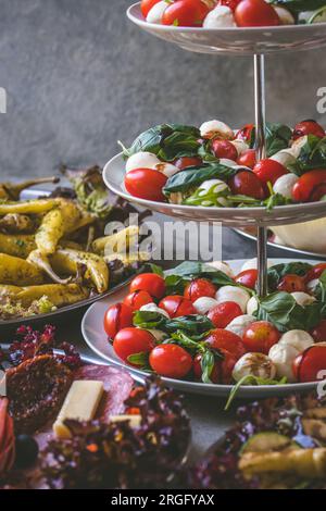Italian starter buffet with tomatoes and mozzarella, grilled pepperoni and sausage specialties, vertical Stock Photo