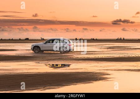 Car that drives through the puddles that occur at low tide on the North Sea beach, beautiful light in the sunset Stock Photo