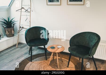 Two cozy dark green velvet armchairs and a wooden coffee table on a round sisal rug Stock Photo