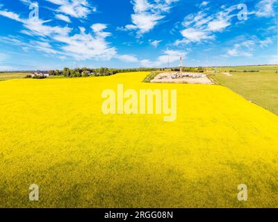 Aerial blooming canola field overlooking an oil and gas drilling rig next to a rural property near the Calgary city limits in Rocky County Alberta Can Stock Photo