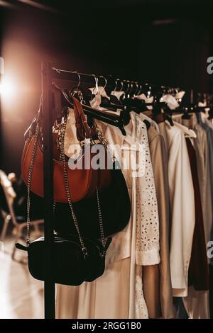Women's white long dresses and handbags with chains hanging on hangers on the fashion backstage Stock Photo