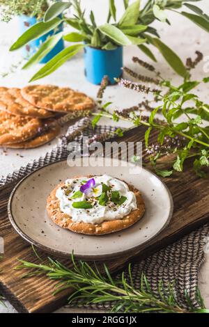 Round crispbread with herbal cream cheese and fresh herbs on a wooden board, vertical Stock Photo