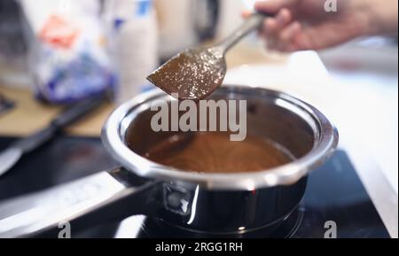 Female hand hold spoon close up and mix cream in kitchen. Stock Photo
