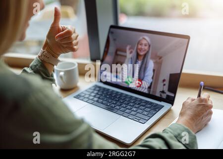 Close up of woman freelancer have video conference with client and making notes sitting near window Stock Photo