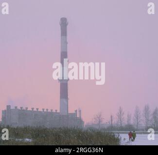 Photo of small people against the background of a large boiler-house chimney during a strong blizzard Stock Photo