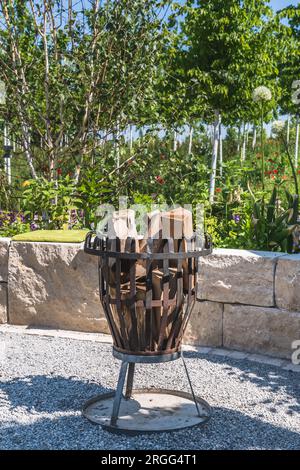 Metal fire basket filled with wood in a garden, vertical Stock Photo