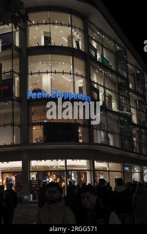 People in front of a Peek & Cloppenburg store at night. Peek & Cloppenburg is an international chain of department stores from Germany, operating in 1 Stock Photo