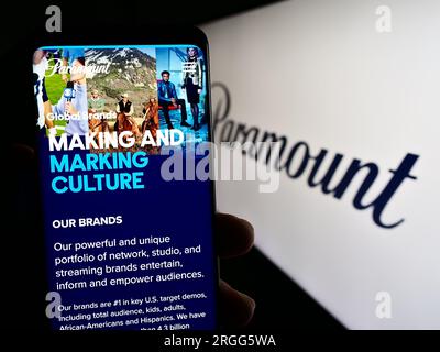 Person holding cellphone with webpage of US entertainment company Paramount Global on screen in front of logo. Focus on center of phone display. Stock Photo