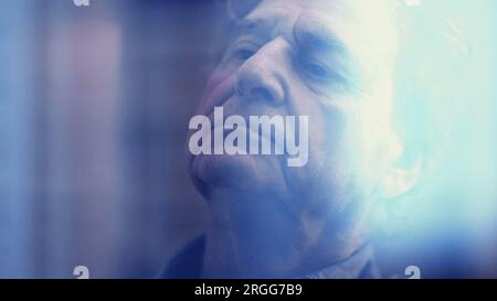 Brooding senior man lost in thought, gazing through his window as the ...