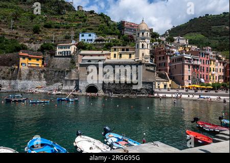 A small harbour front with moored fishing boats near a small Piazza (Square) filled with a mix of eateries, ice cream parlours and the prominent Santa Stock Photo