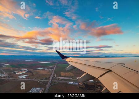 Airplane flight in sunset sky over city and wing of plane. View from the window of the Aircraft. Traveling in air. Stock Photo