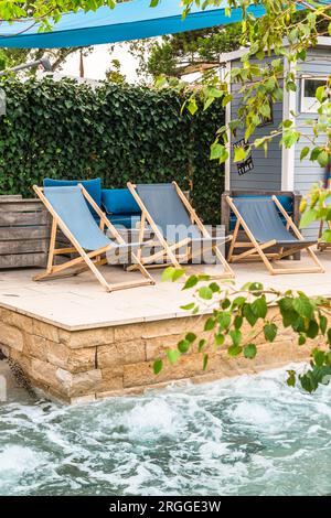 Terrace with sun loungers by modern built-in swimming pool. Bubbling swimming pool, spa area, vertical Stock Photo