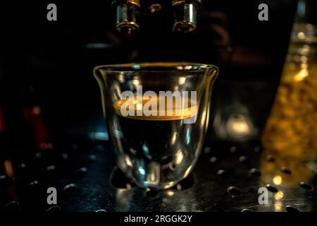 Glass cup with freshly brewed black coffee with foam and golden cream with bubbles visible through the transparency of the cup from a fully automatic Stock Photo