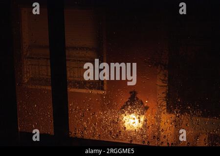 Raindrops on the window glass. Selective focus. Condensation on the transparent glass window, In the background a street light and a window. Sad day. Stock Photo