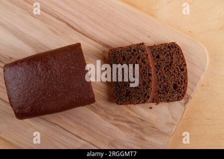 Loaf and slices of dark bread on light beige wooden background Stock Photo