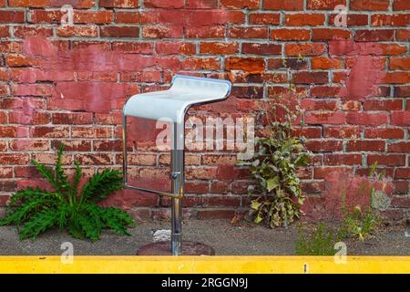 Abandoned chrome stool by a weathered red brick wall Stock Photo