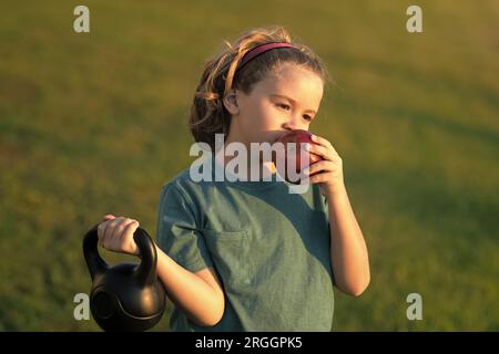 Sporty kid with apple and kettlebell outdoor in summer park. Kids sports exercises. Healthy kids life and sport concept. Motivation and sport concept Stock Photo