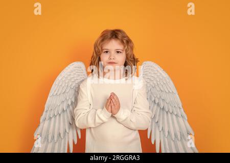 Angel prayer kids. Valentine's day. Blonde cute child with angel wings on a yellow studio background. Happy angel child Stock Photo