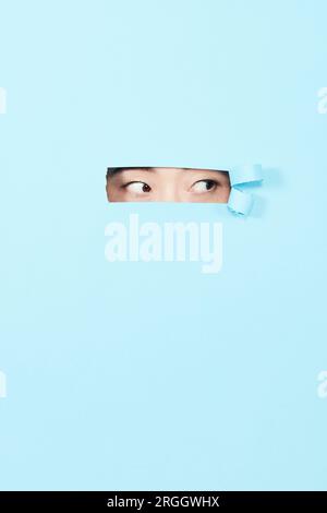 Young woman peeking through cutout in blue paper Stock Photo