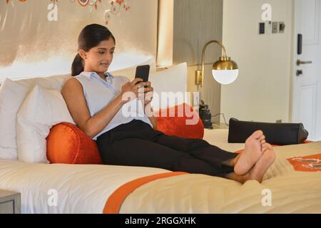 Businesswoman using smart phone on hotel room bed Stock Photo