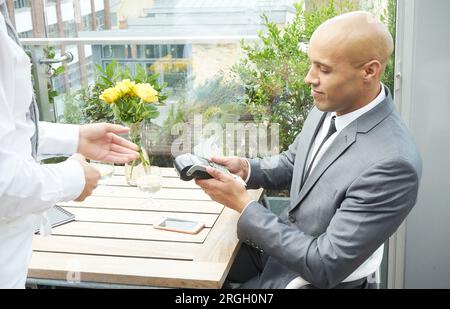 Businessman using EFTPOS machine at restaurant table Stock Photo