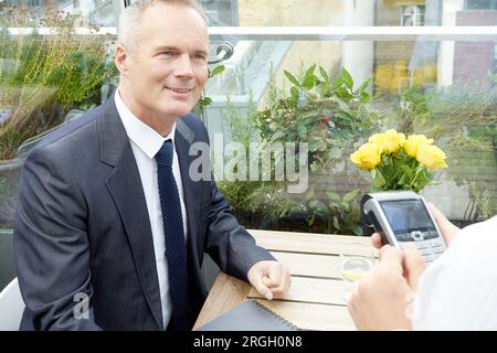 Businessman using EFTPOS machine at restaurant table Stock Photo